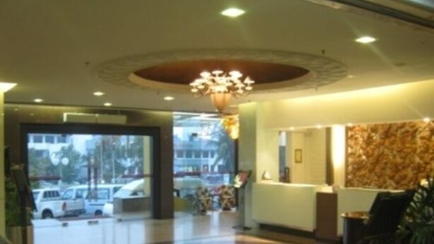 A hotel lobby with a reception desk, a chandelier, and a view of parked cars outside.