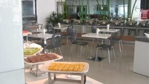 A modern dining area with tables and chairs, a buffet with various food items, and decorative plants.