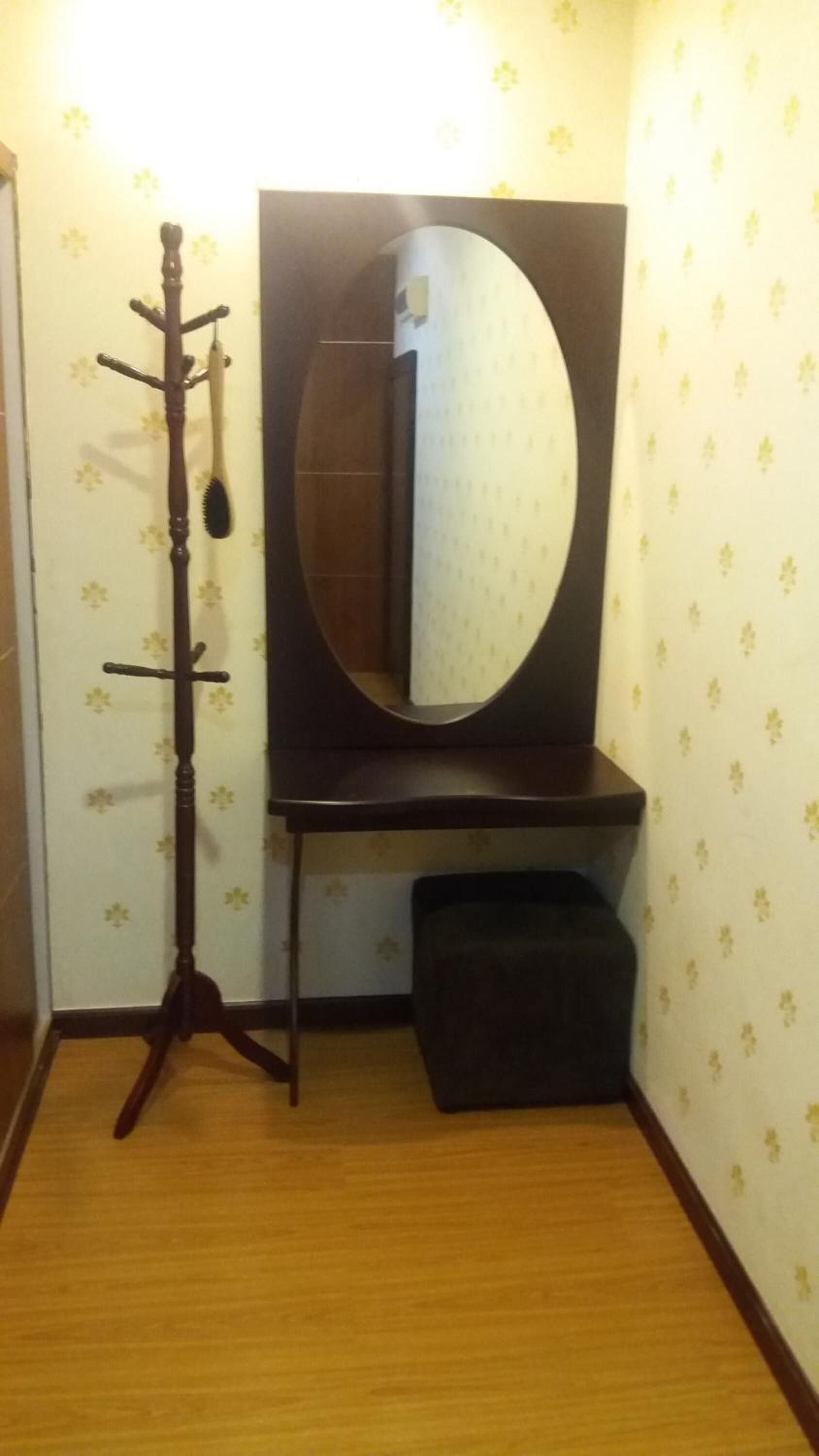 A bathroom with a wooden coat rack, a large mirror, and a small bench.