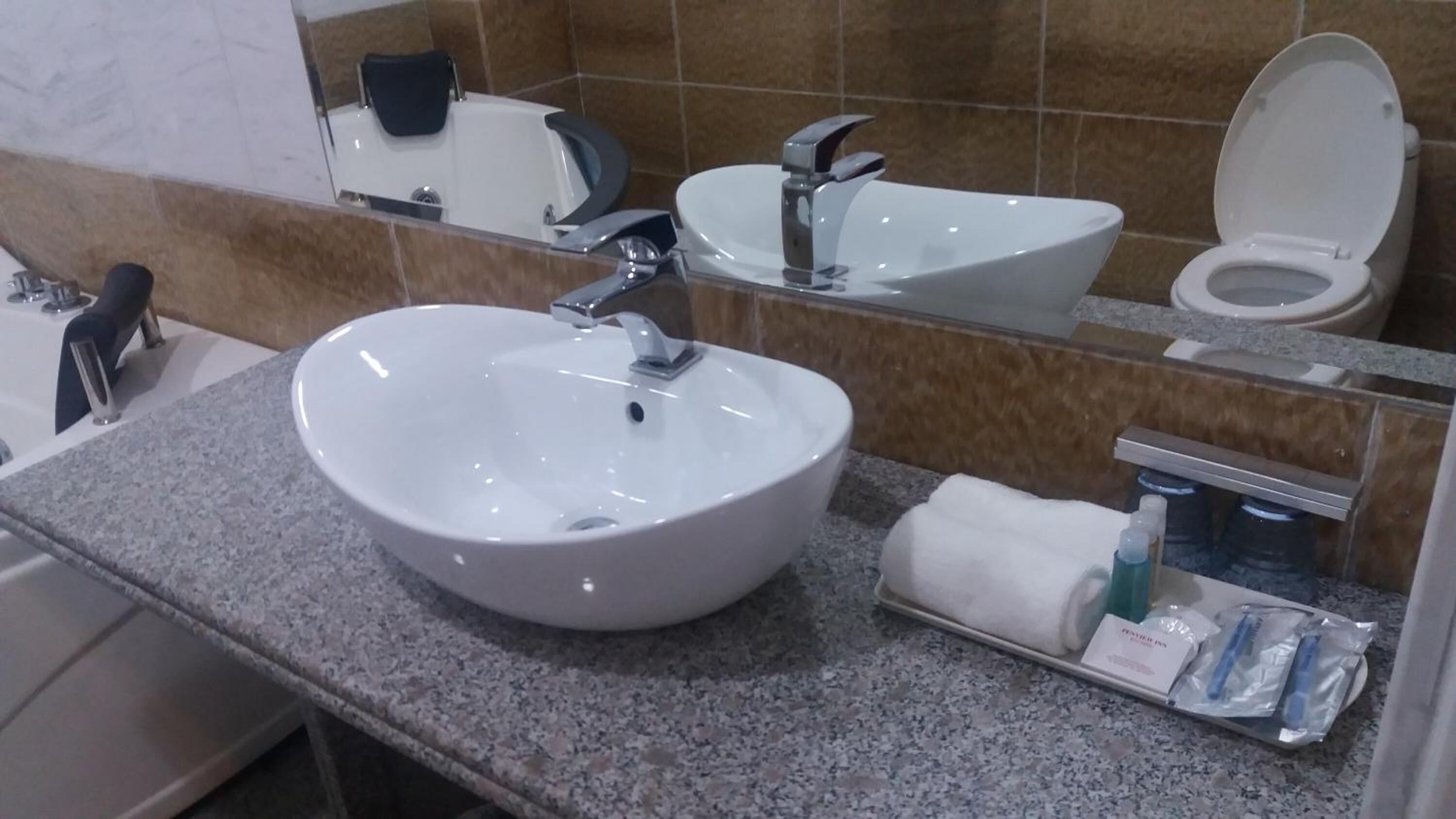 Un baño con lavamanos blanco, espejo, inodoro y toallero con artículos de aseo.