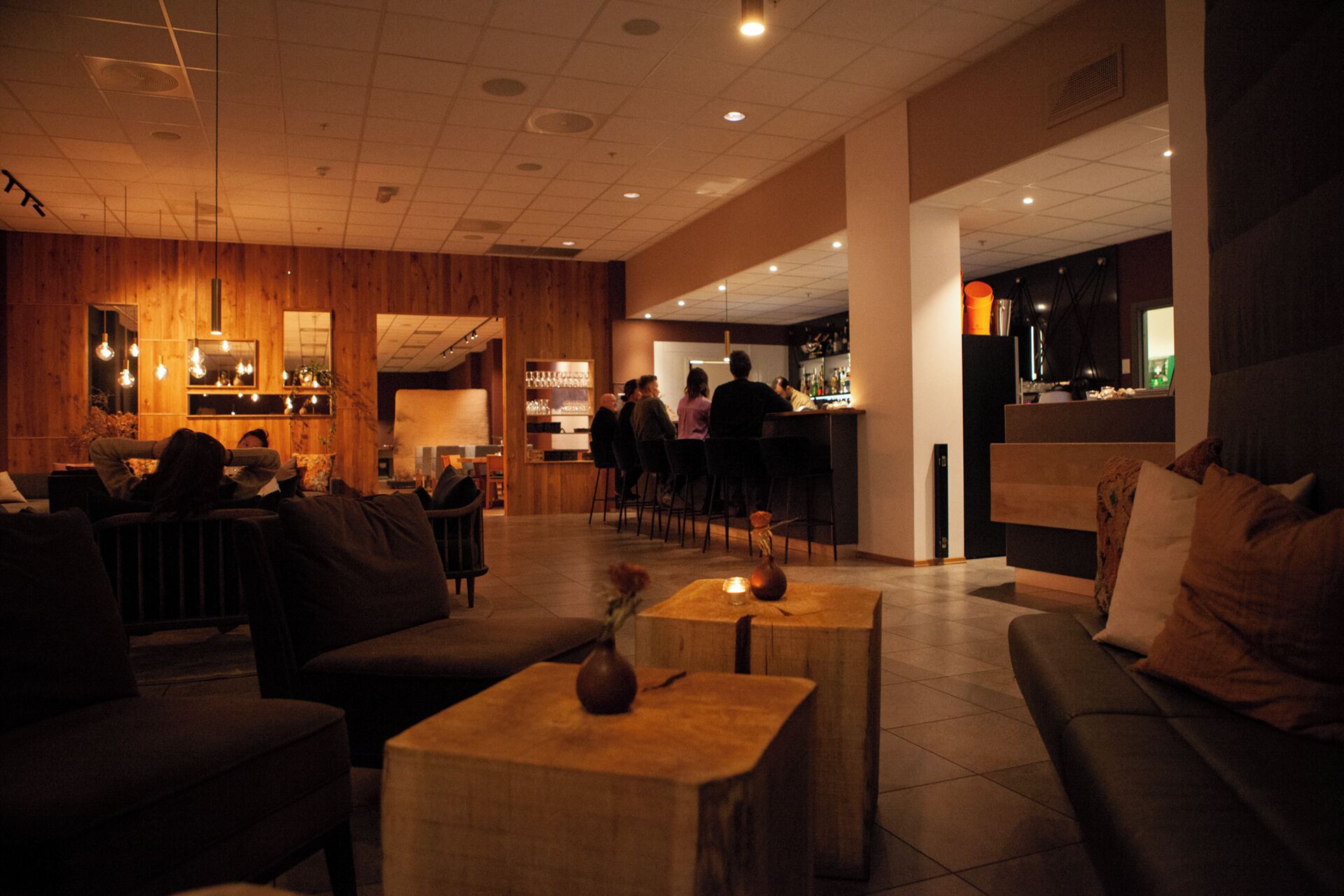 Zona de bar con mobiliario de madera, barra y área de estar con sofás y mesas.