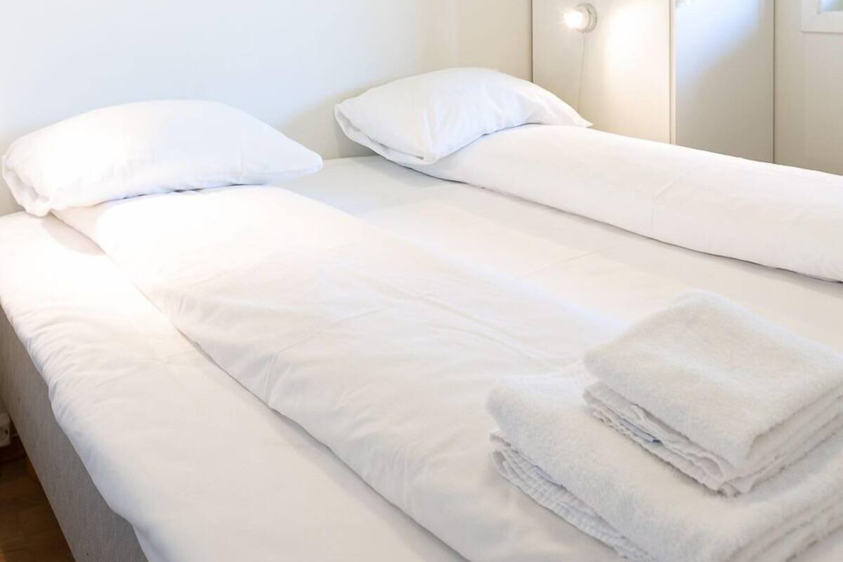 A room with two beds, white bedding, a wardrobe, and a window.