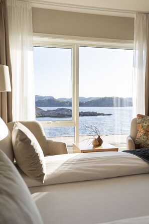 A hotel room with a large window offering a view of a coastal landscape.