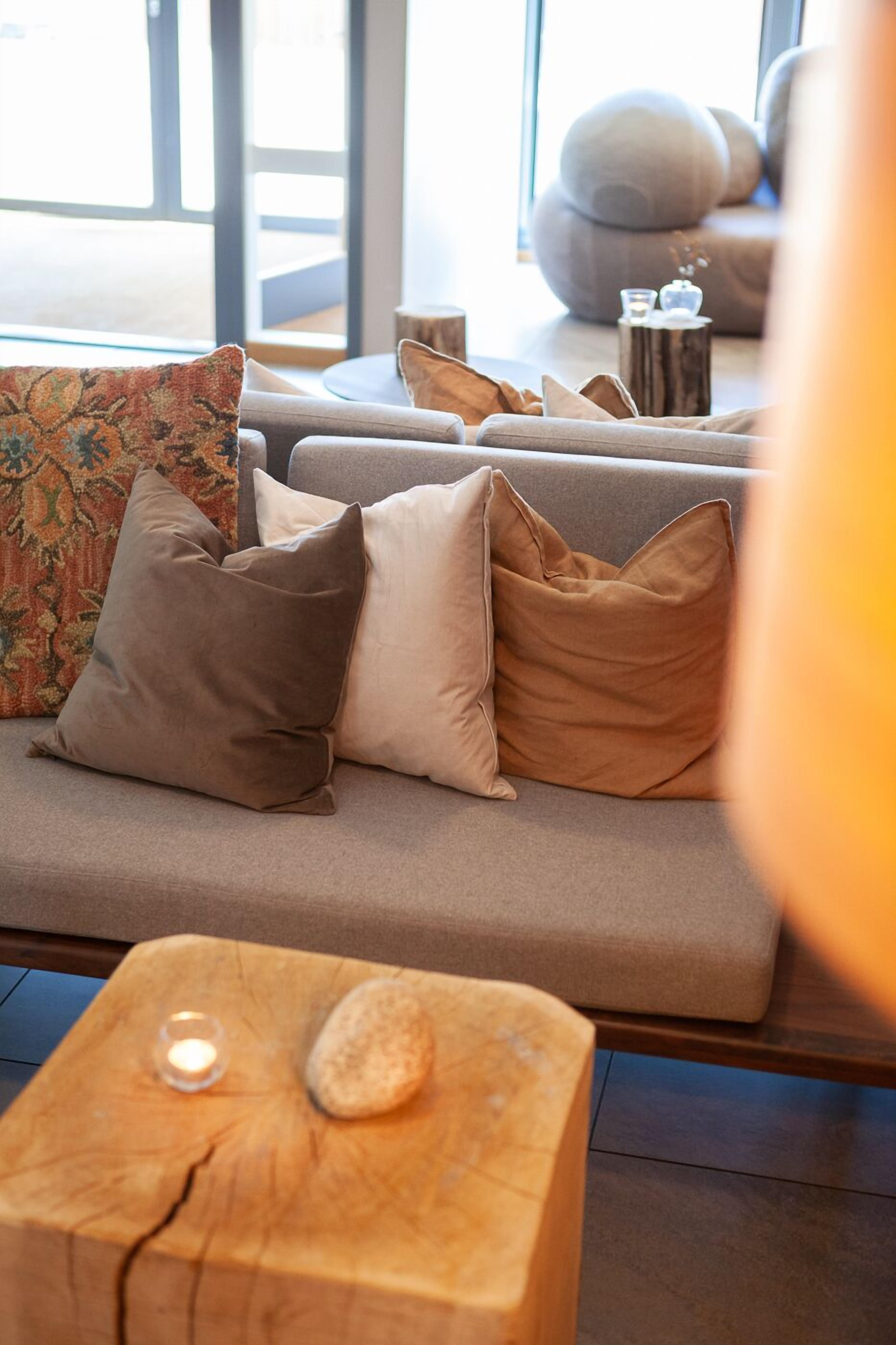 Una sala moderna con un sofá gris, varios cojines y una mesita de madera con una vela.