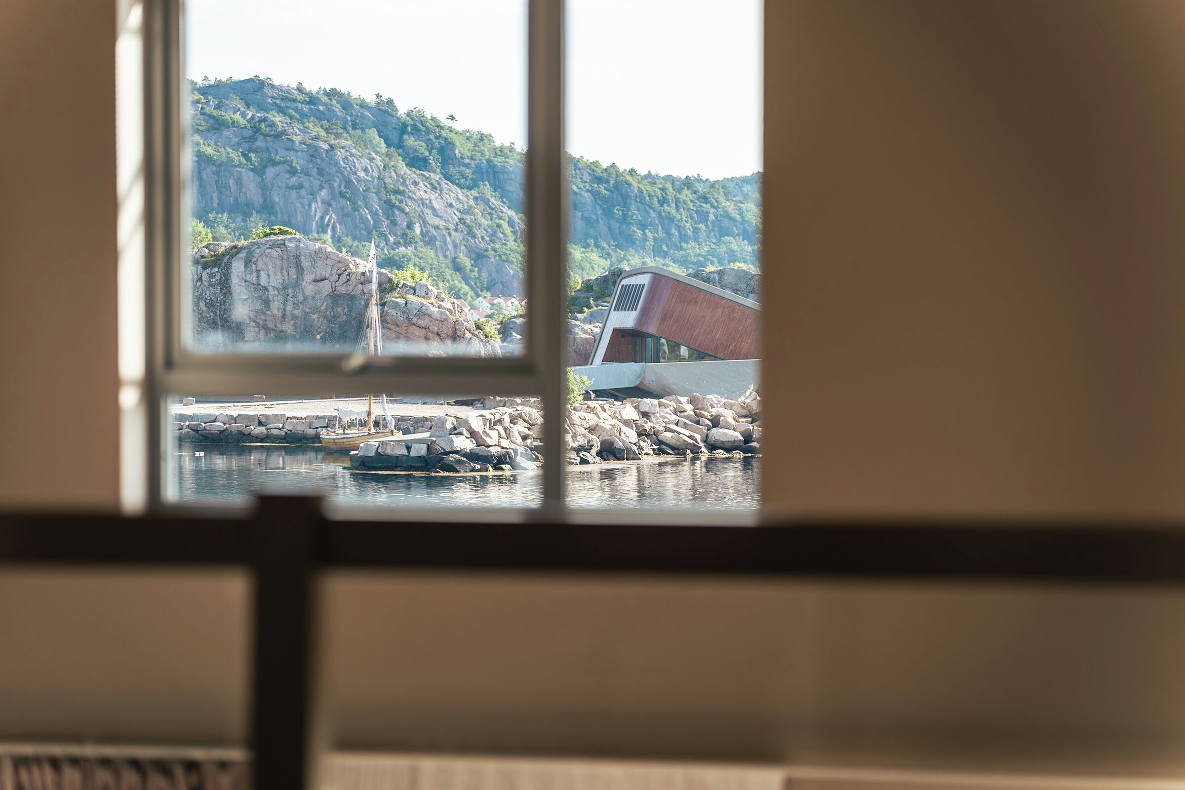 A view through a window of a building with a rocky landscape and a dock with boats.