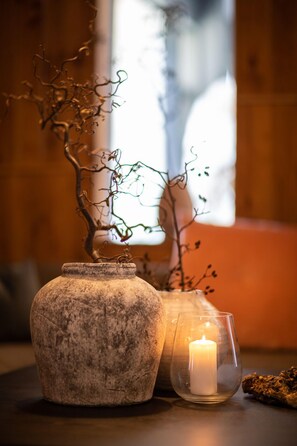A stone vase, a candle in a glass holder, and a branch with leaves on a table.