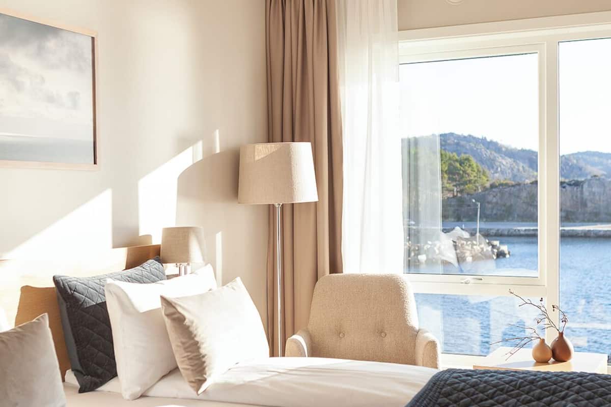 A hotel room with a bed, a chair, a lamp, and a view of a body of water.