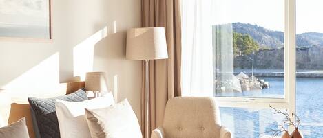 Habitación de hotel con cama, una silla, una lámpara, un cuadro y vista al mar.
