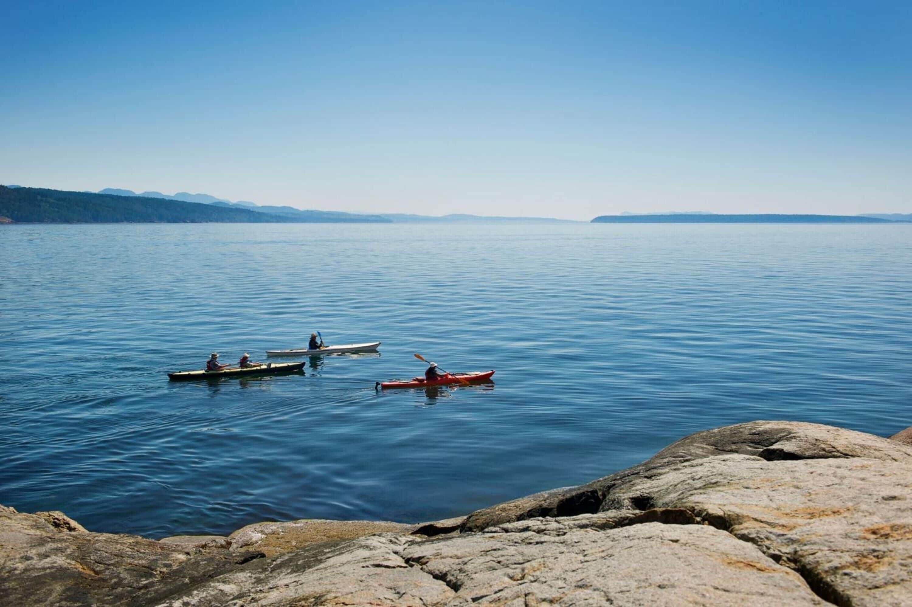 A calm lake with three kayaks on the water, surrounded by rocky shores.