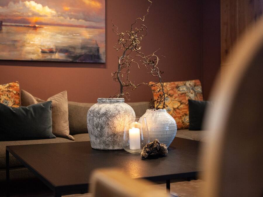 A living room with a sofa, two vases, a candle, and a painting on the wall.