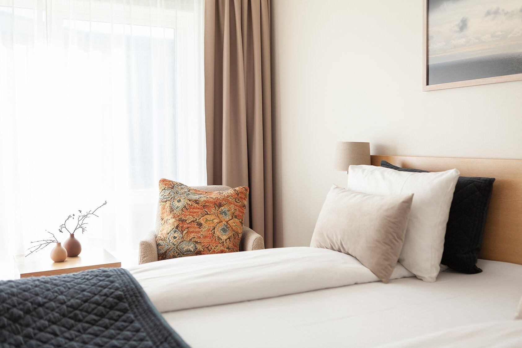 A hotel room with a bed, a chair, a nightstand, a lamp, and a window with curtains.