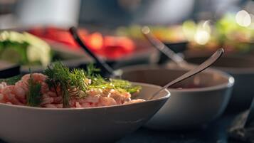 A bowl of shrimp garnished with dill, a spoon, and a blurred background of other food items.