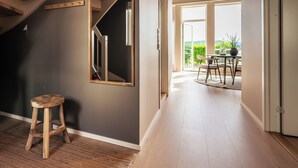 Una escalera con vigas de madera, un taburete de madera y vistas a un balcón exterior con mesa y sillas.