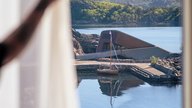 Vista de un lago tranquilo con un bote, un edificio y un paisaje montañoso.