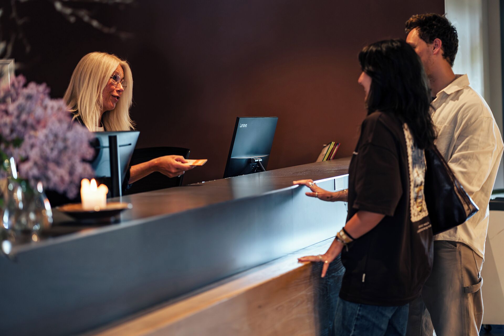 A reception desk with a laptop, a vase with flowers, and a candle.