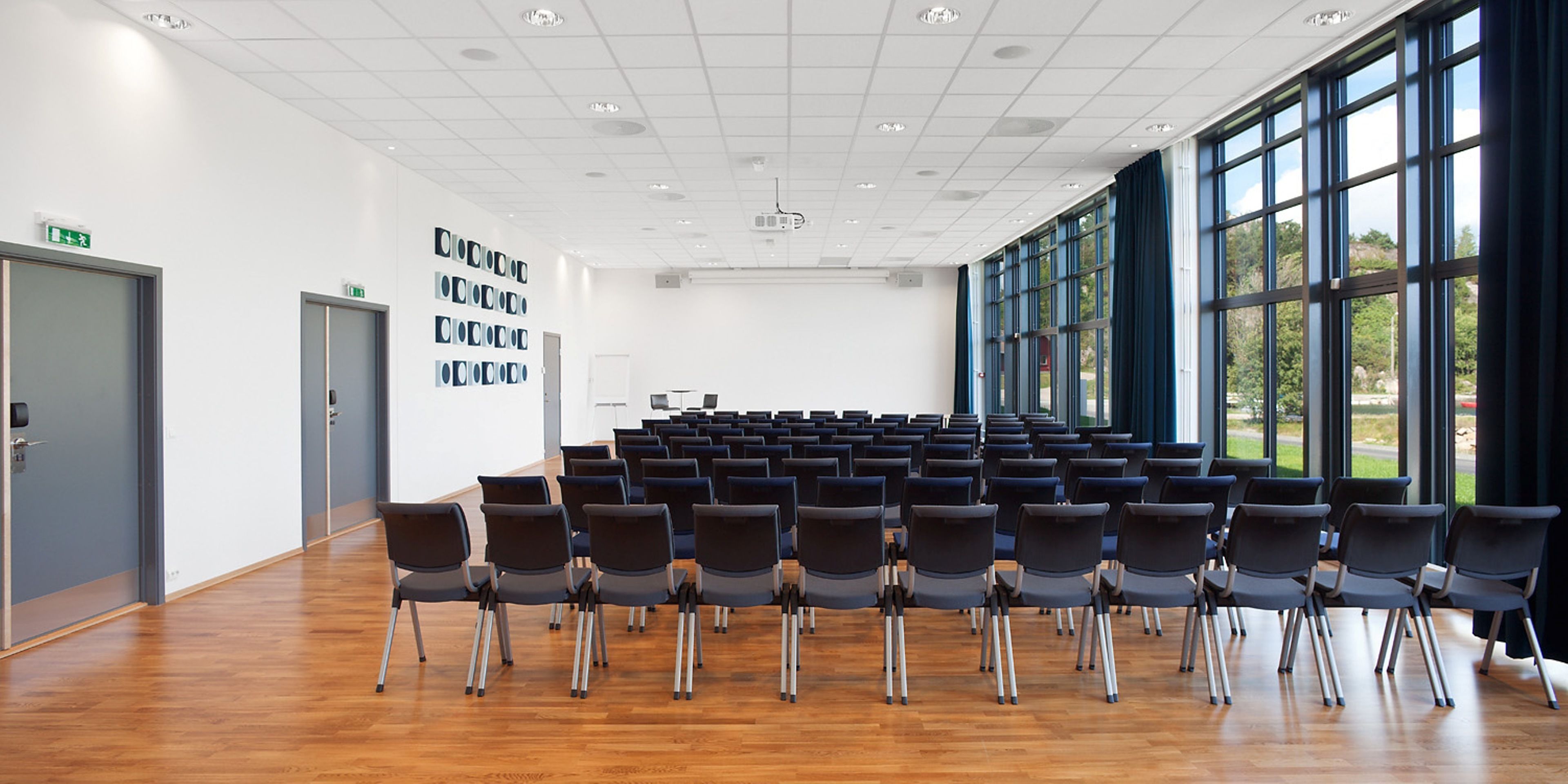 A conference room with rows of chairs, large windows, and a wooden floor.