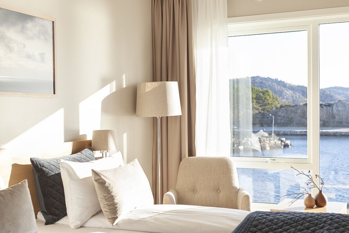 Habitación de hotel con una cama, una silla, una lámpara y vistas a un cuerpo de agua.