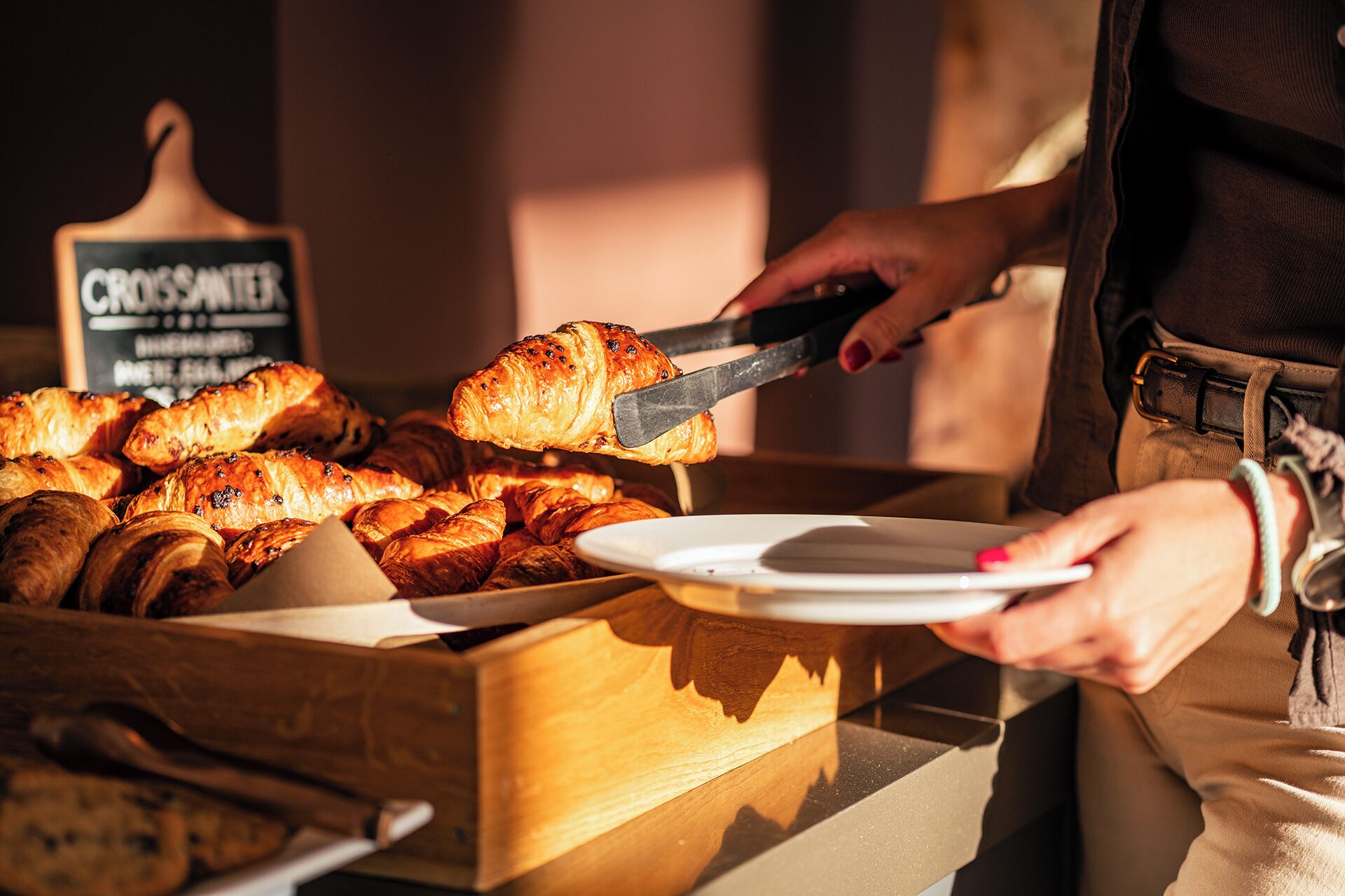 A person serving croissants from a wooden box.