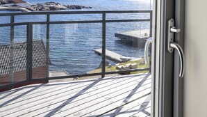Una terraza de madera con vista a un cuerpo de agua tranquilo y colinas distantes.