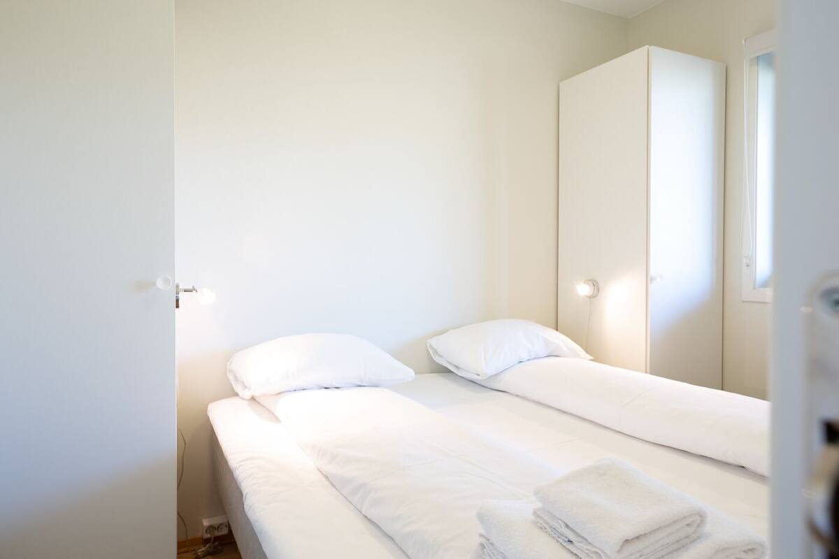 A small, clean room with two beds, a wardrobe, and a window.