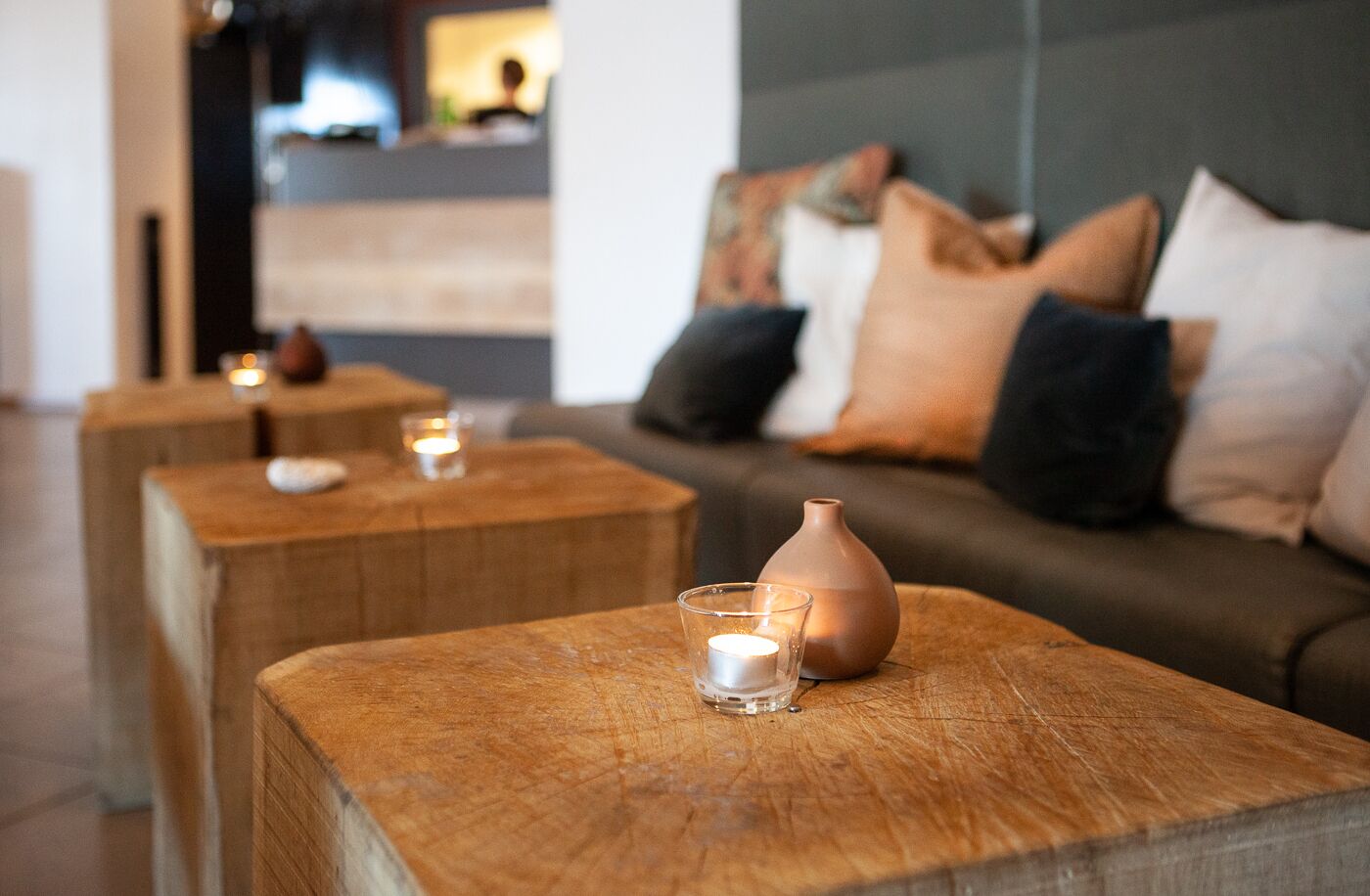 Ein gemütlicher Wohnbereich mit einer Couch und drei Holznachttischen, auf jedem Tisch eine Kerze und eine Vase.