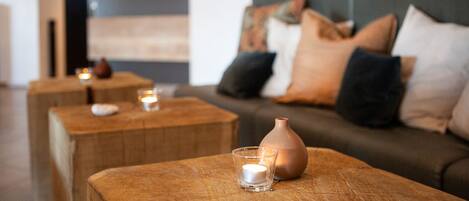 Un salon chaleureux avec un canapé et trois petites tables en bois, chacune agrémentée d’une bougie et d’un vase.