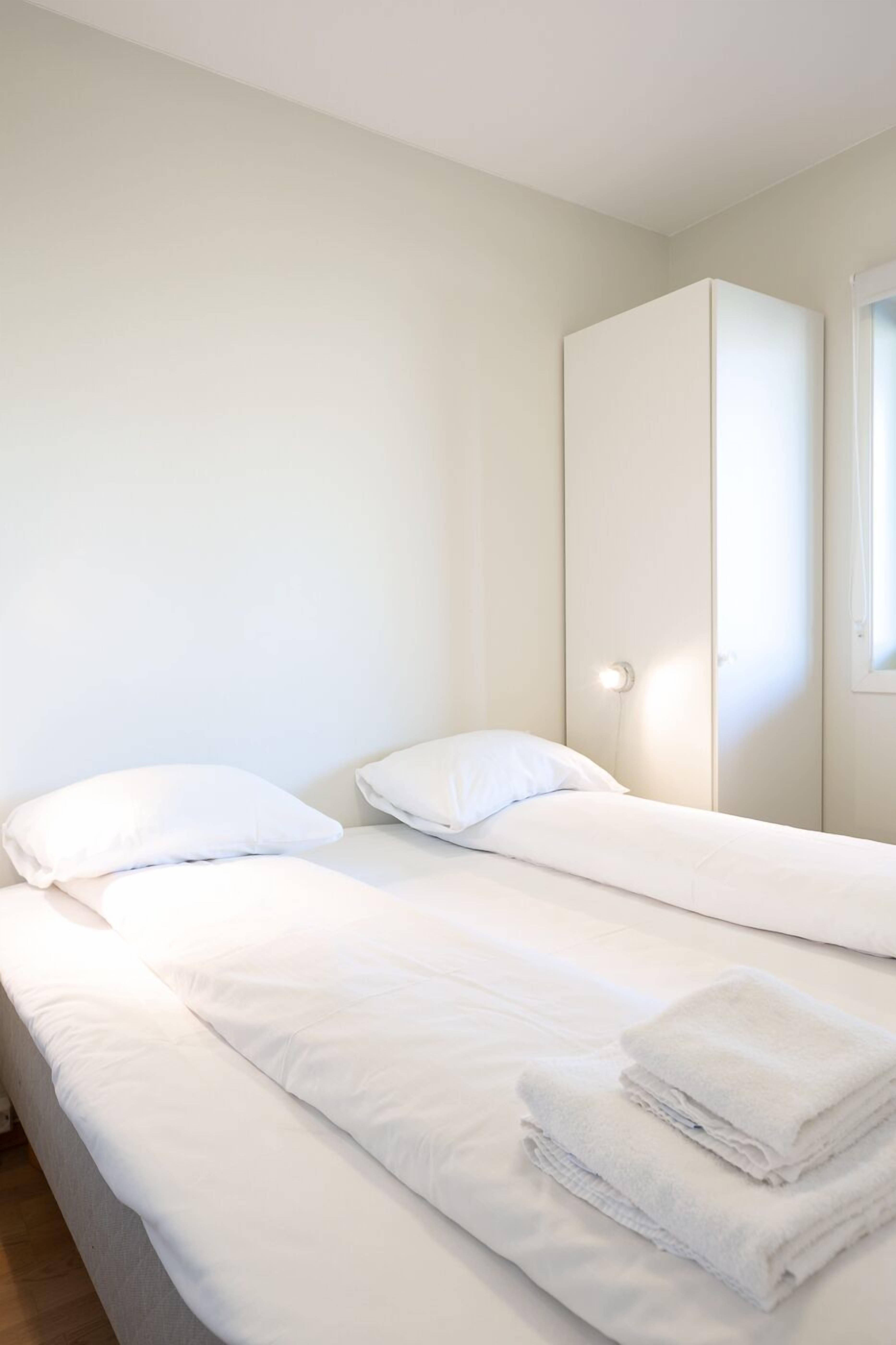 Una habitación con dos camas, ropa de cama blanca y un armario.