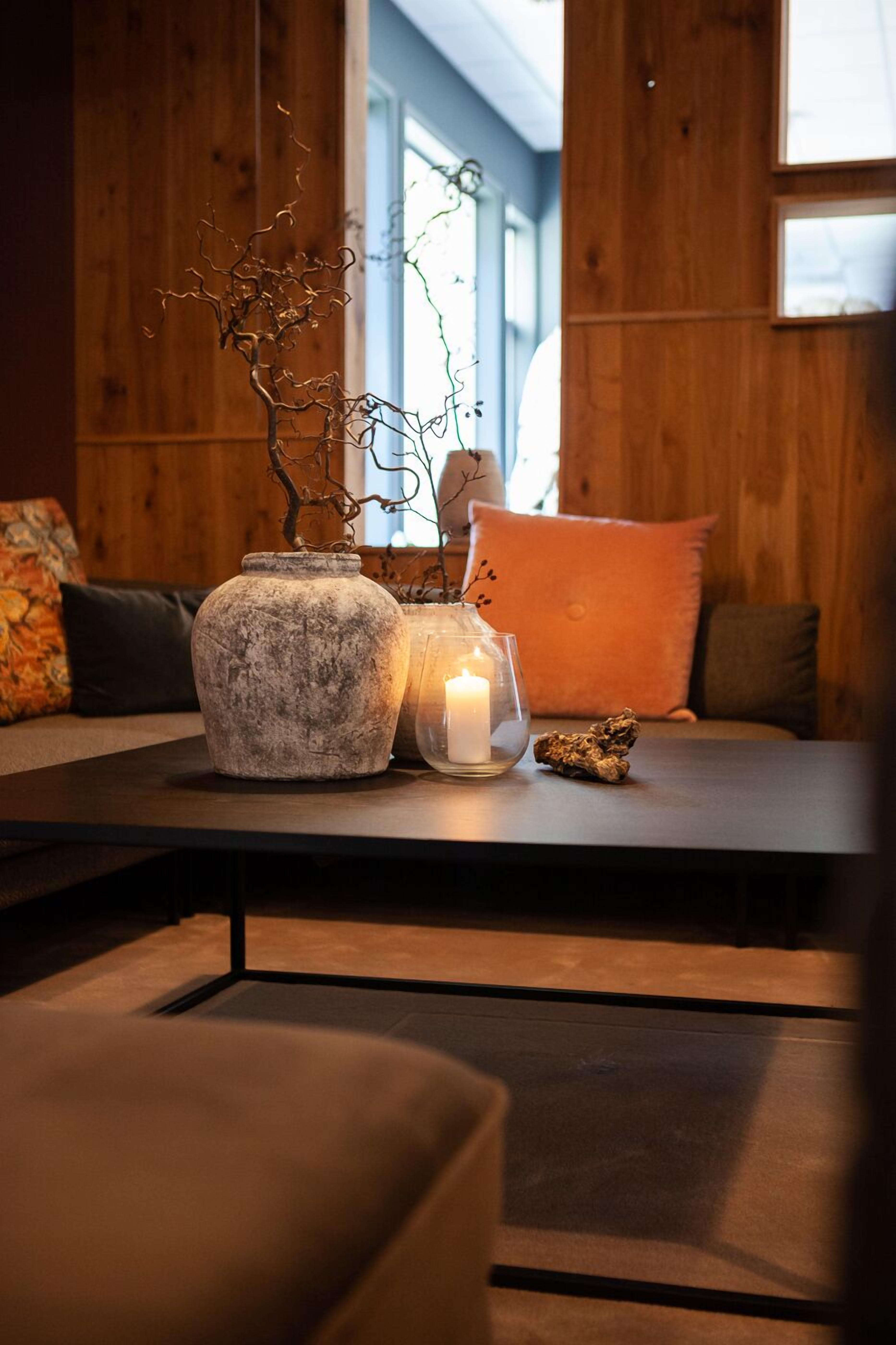 A wooden interior with a table displaying a vase, a candle, and a branch.