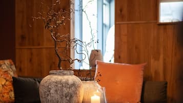 A wooden interior with a table displaying a vase, a candle, and a branch.