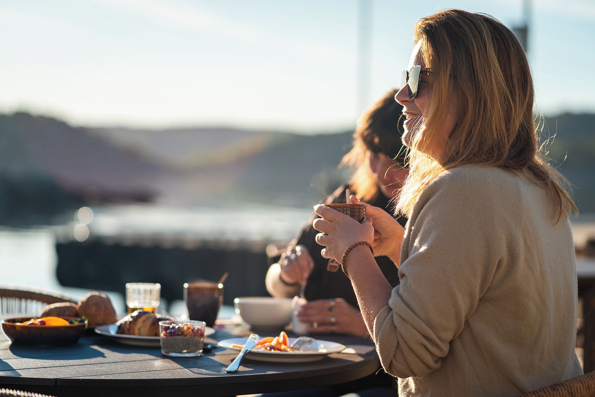 Une table à manger, dressée avec des plats et des boissons, donnant sur une étendue d’eau.