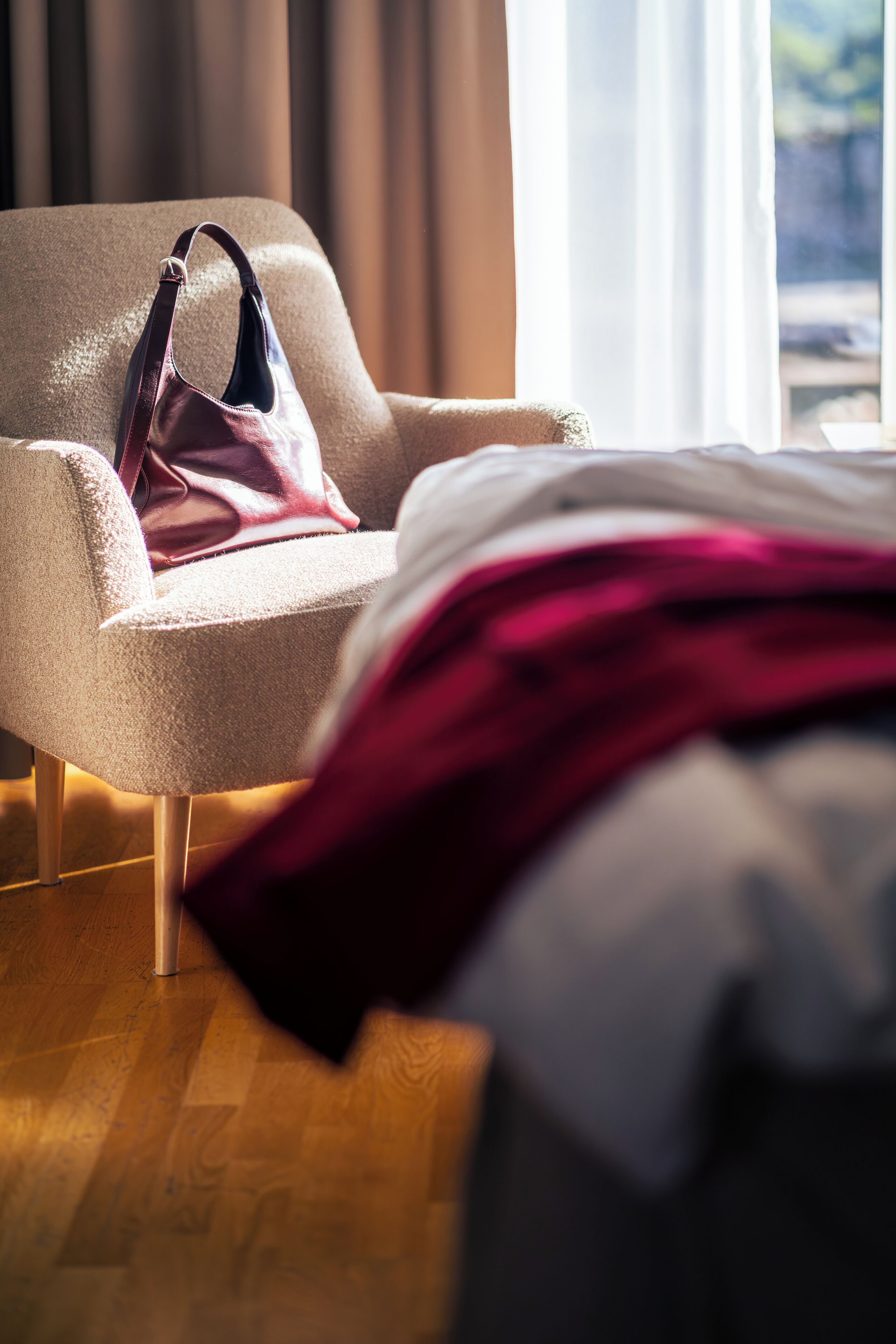 A hotel room with a bed, a chair, and a handbag on the floor.