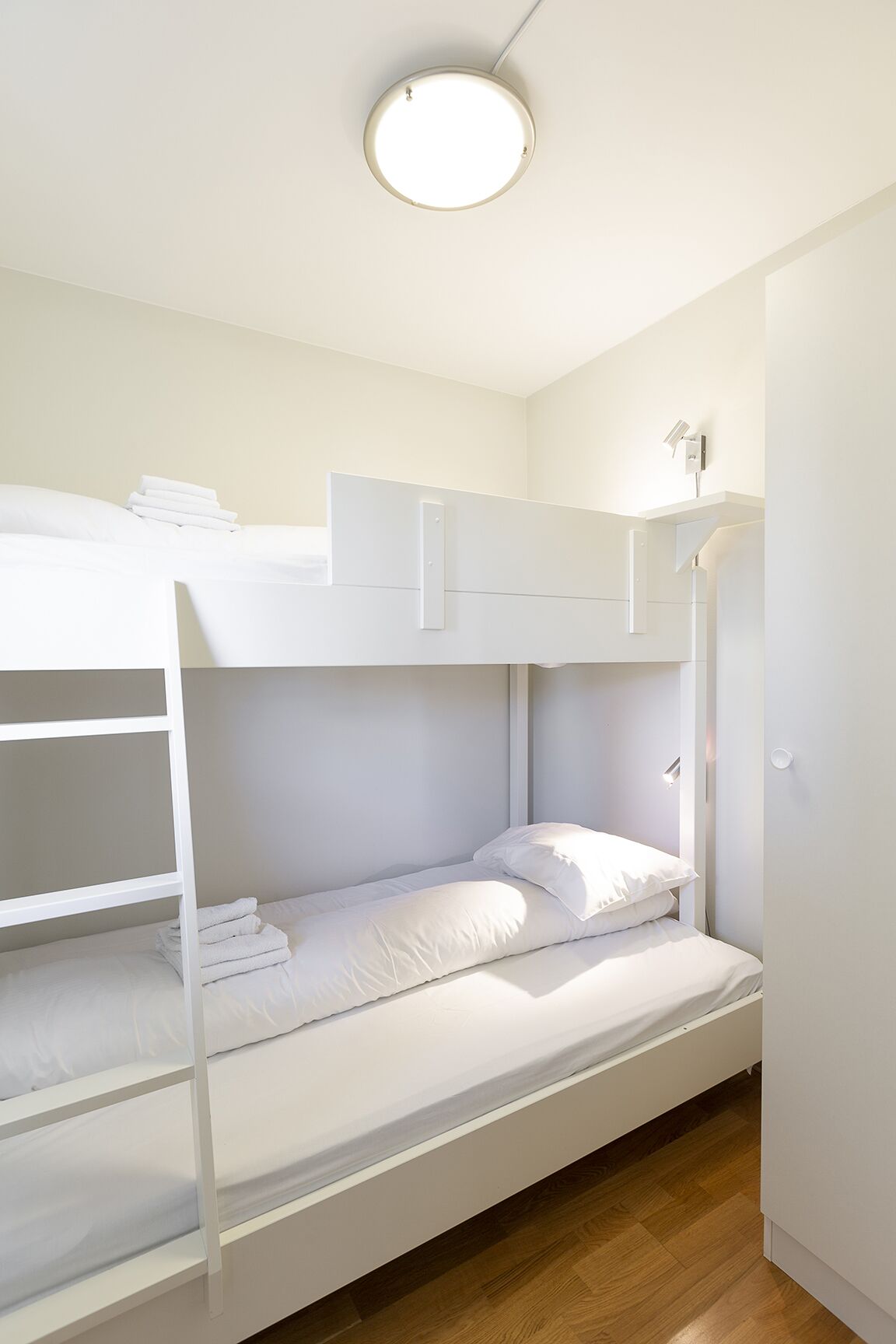 Quarto com beliche, roupa de cama branca e luminária no teto.