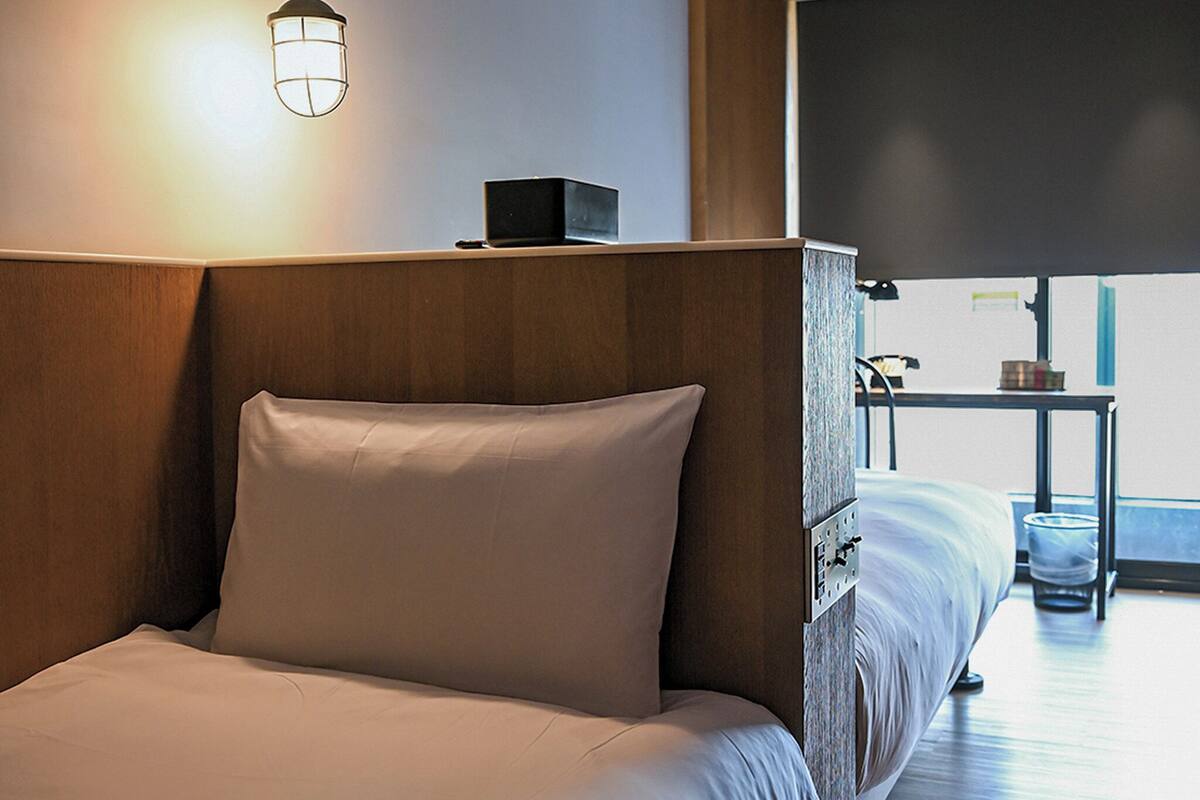 Una habitación de hotel con una cama, una mesita de noche, una lámpara y vistas al exterior.