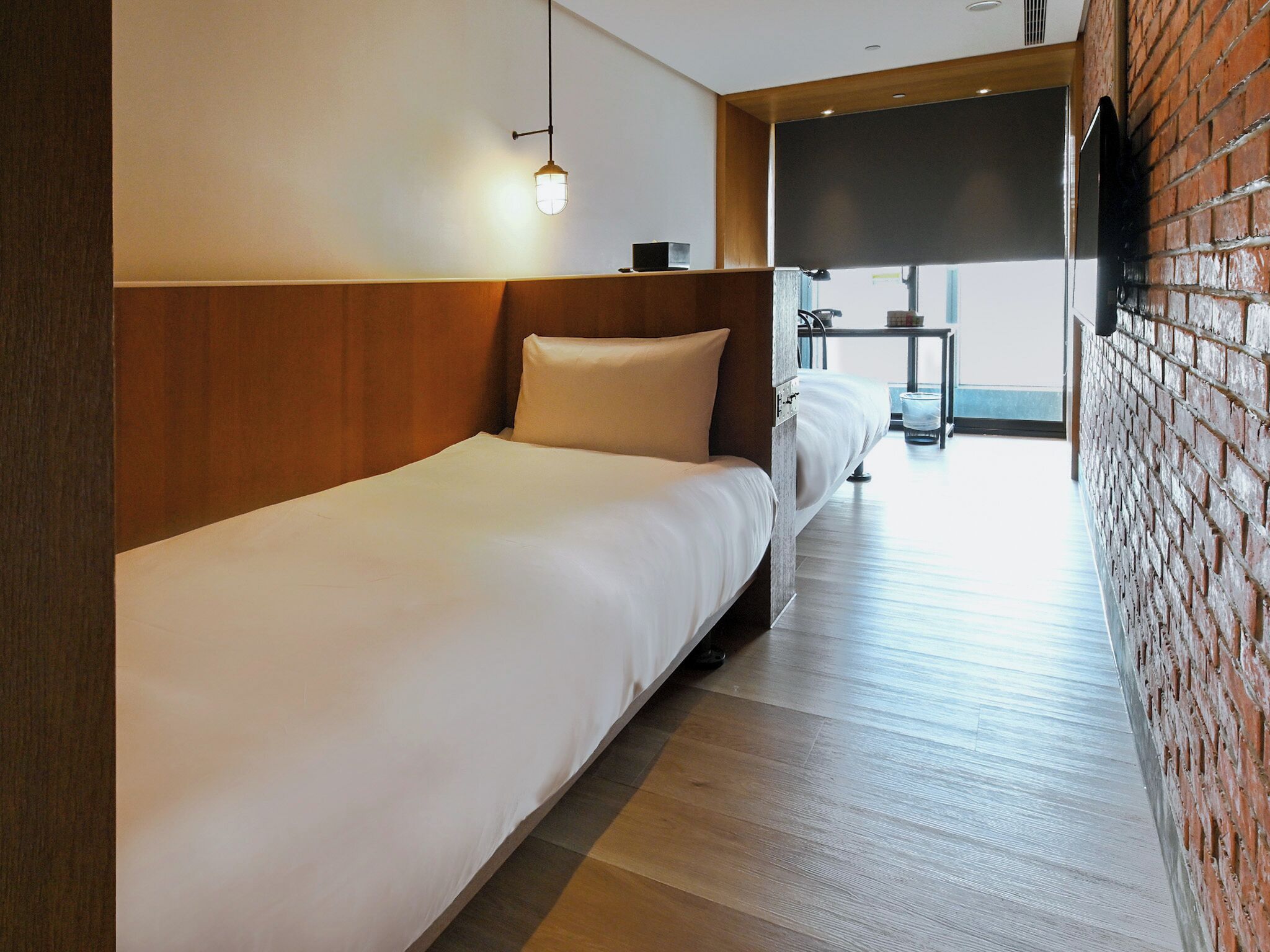 Ein Hotelzimmer mit einem Einzelbett, einem hölzernen Kopfteil, einem kleinen Tisch und einem an der Wand befestigten Fernseher.