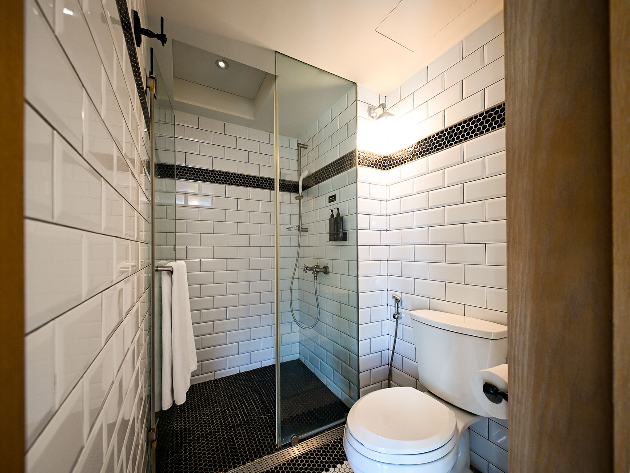 A modern bathroom with white subway tiles, a glass shower enclosure, a toilet, and a black and white patterned floor.