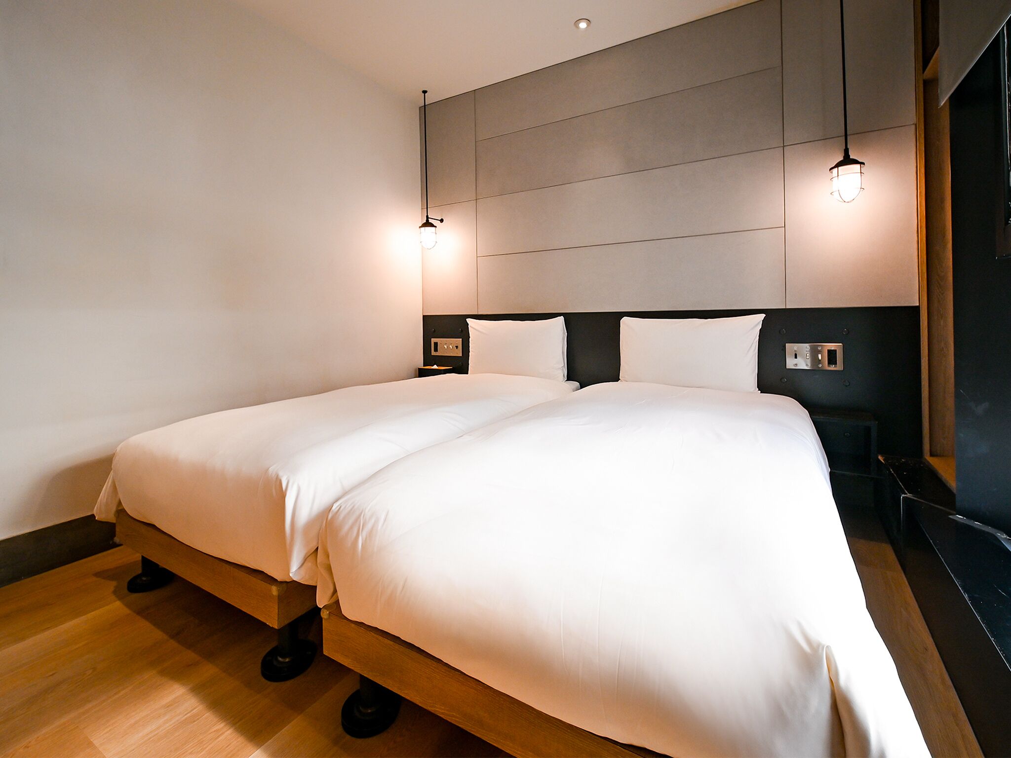 A modern hotel room with a large bed, wooden flooring, and a minimalist design.