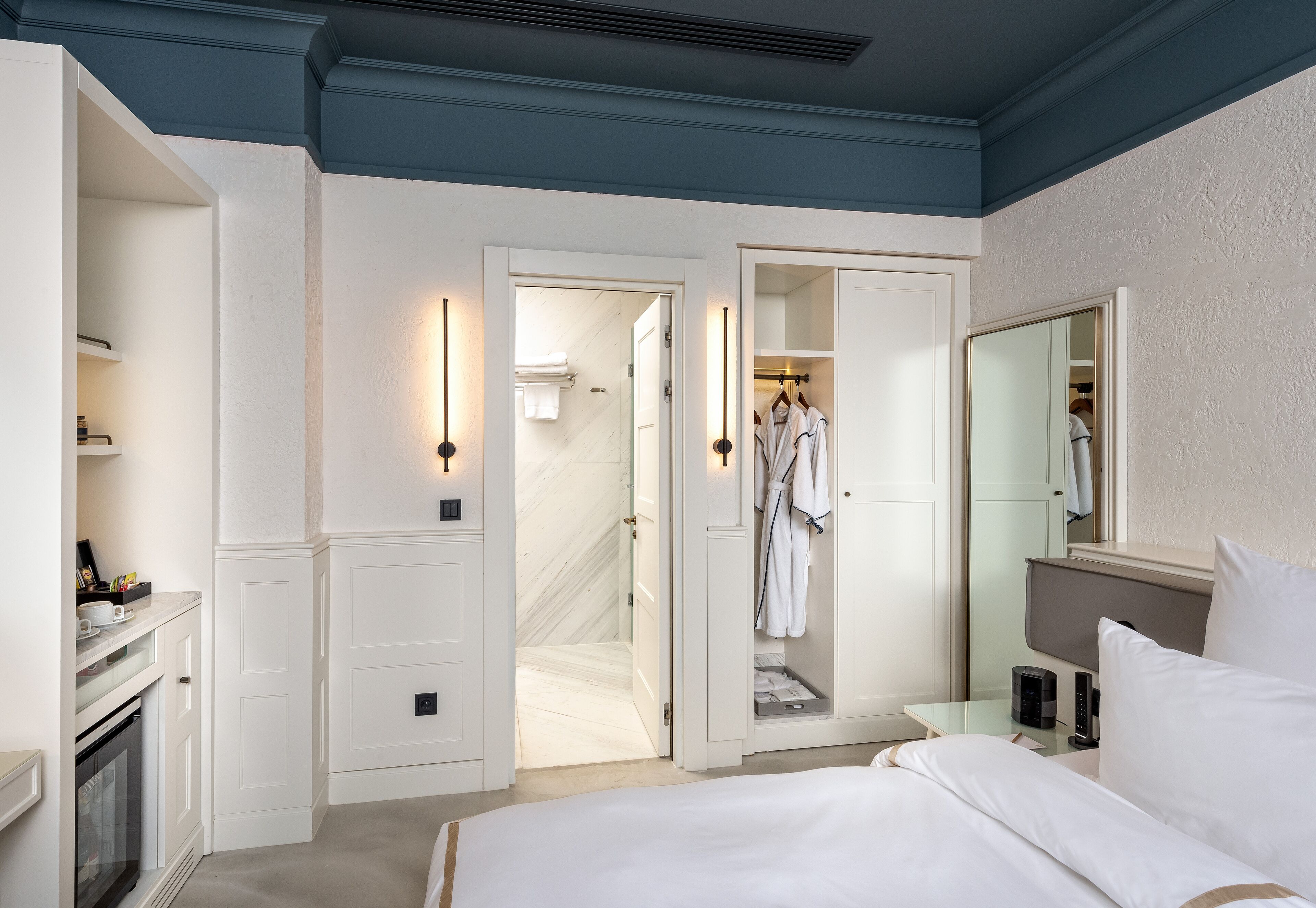 Habitación de hotel con cama, tocador con espejo, vestidor y baño con ducha.