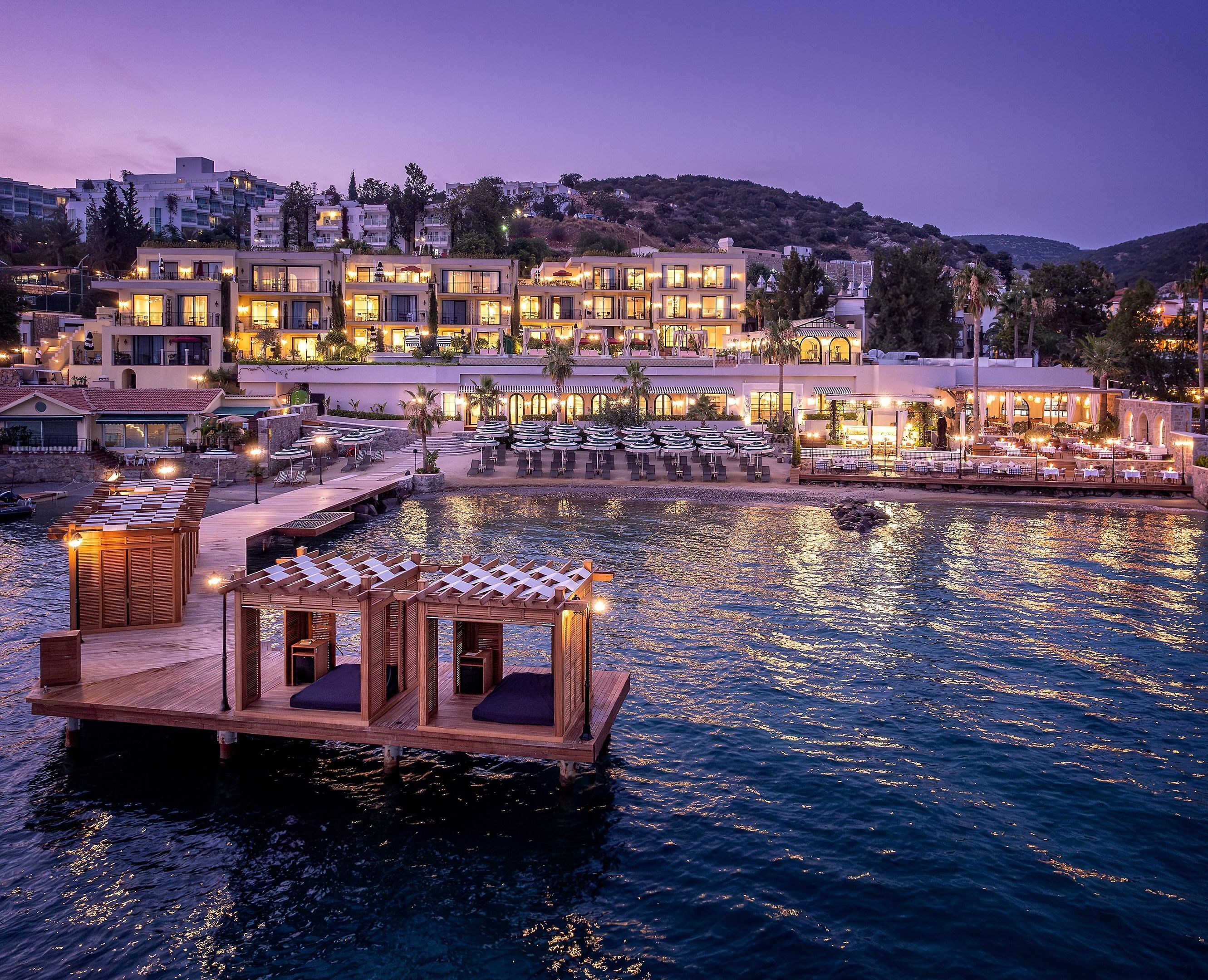 Un hotel frente al agua con varias zonas de comedor, un bar junto a la piscina y una estructura de barco de madera.
