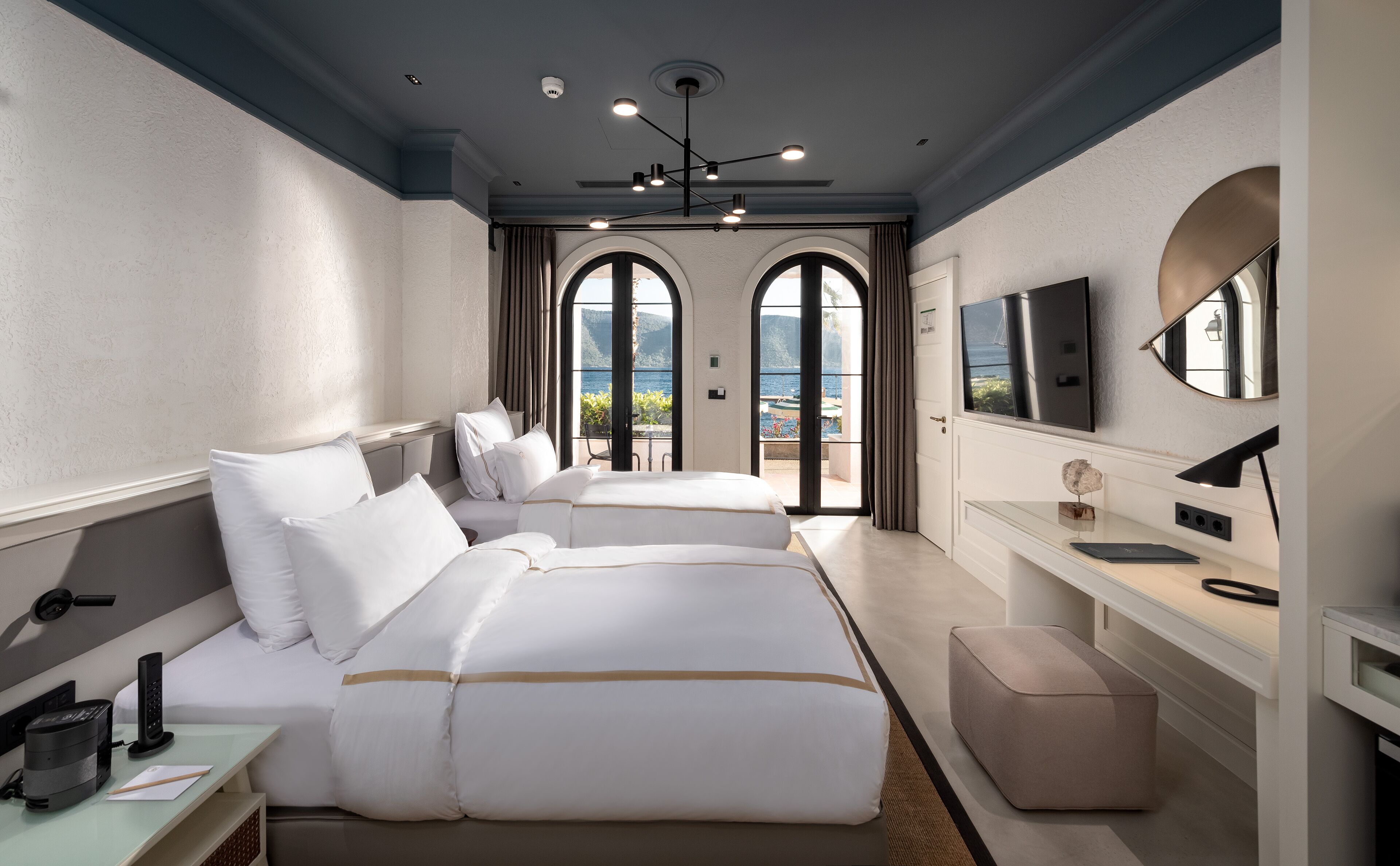 Habitación de hotel con dos camas, un escritorio, una silla, un televisor y vista al mar.