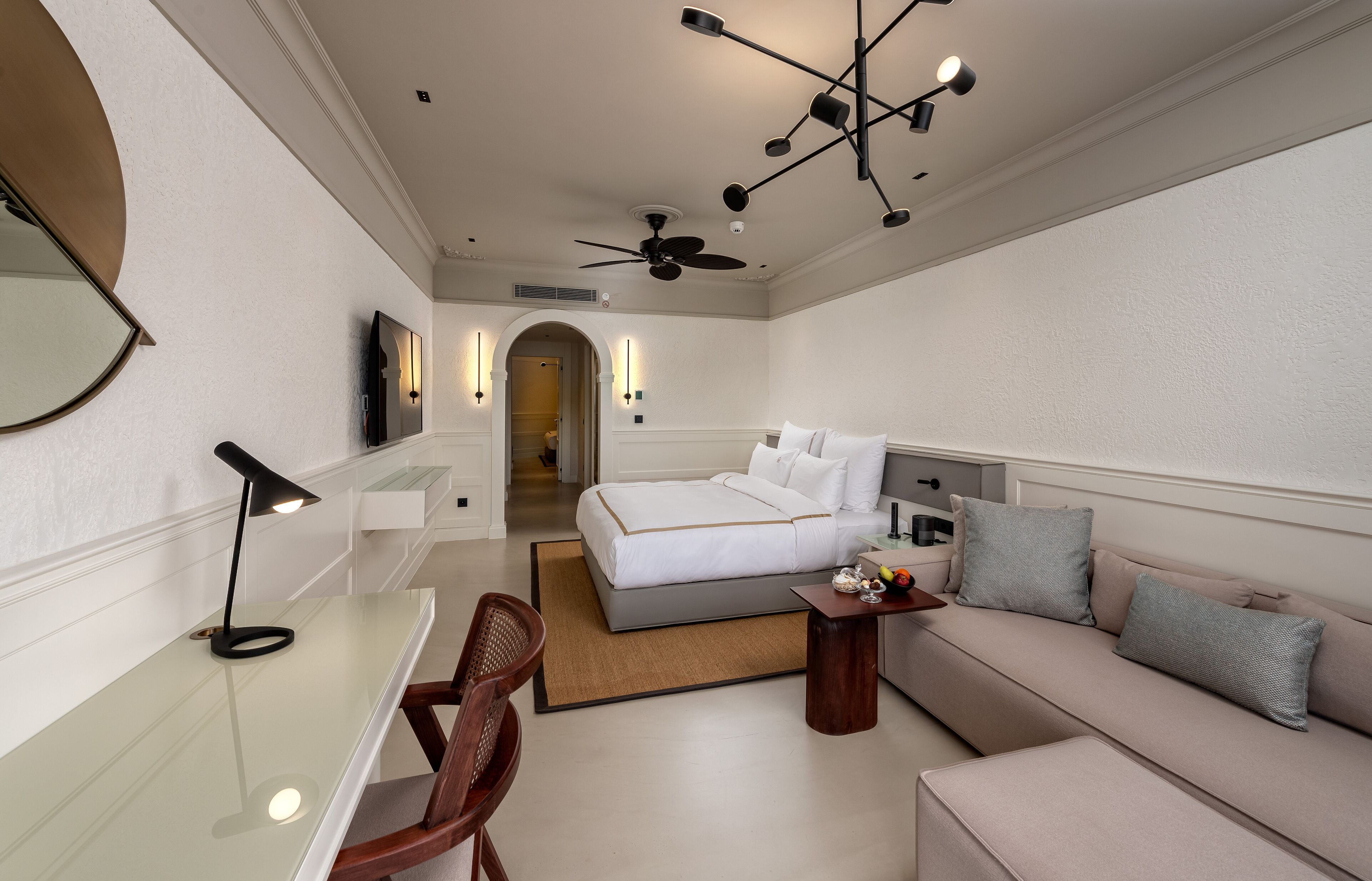 A modern hotel room with a bed, sofa, desk, and chair.