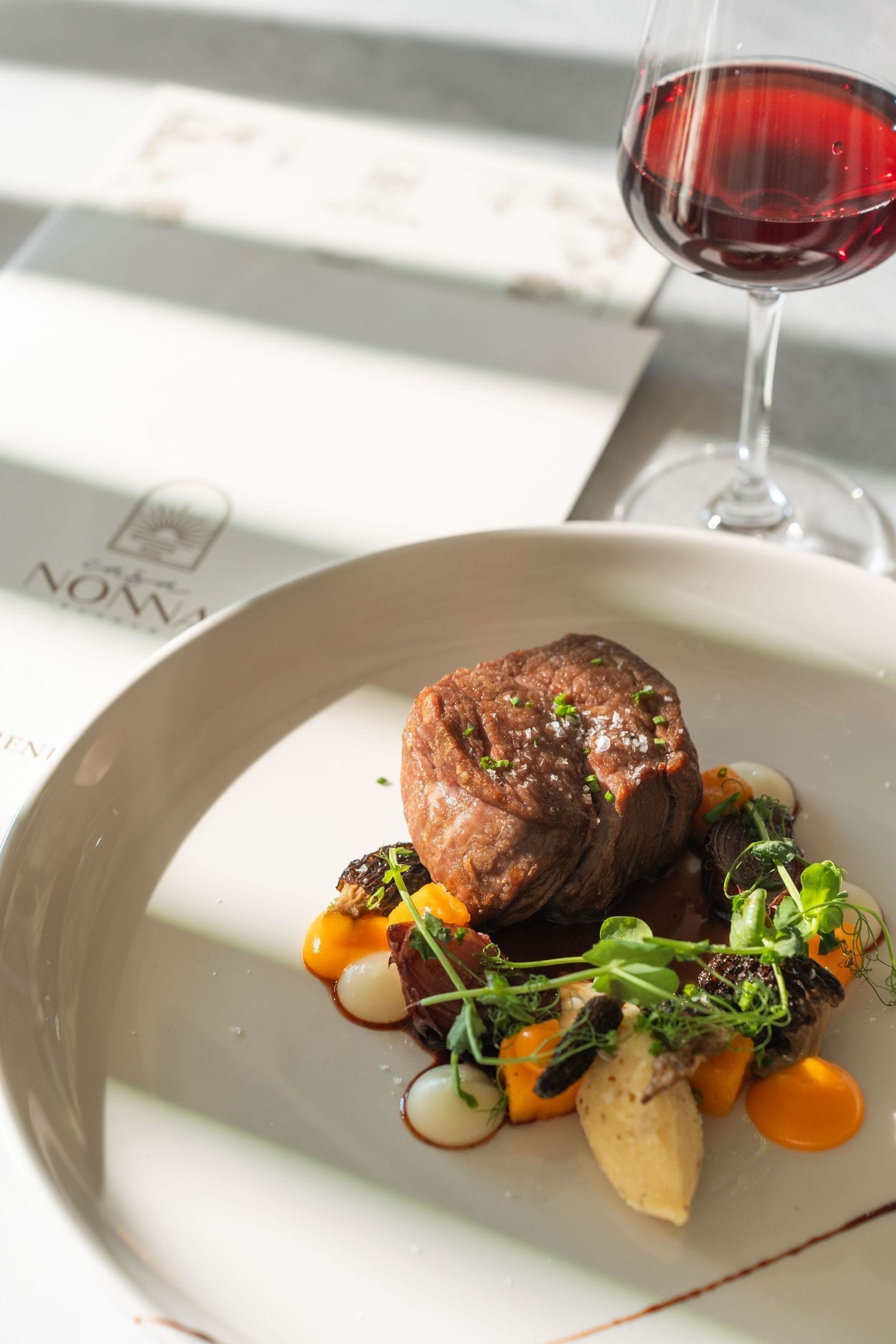 A plate of food with a piece of meat, vegetables, and a glass of red wine.