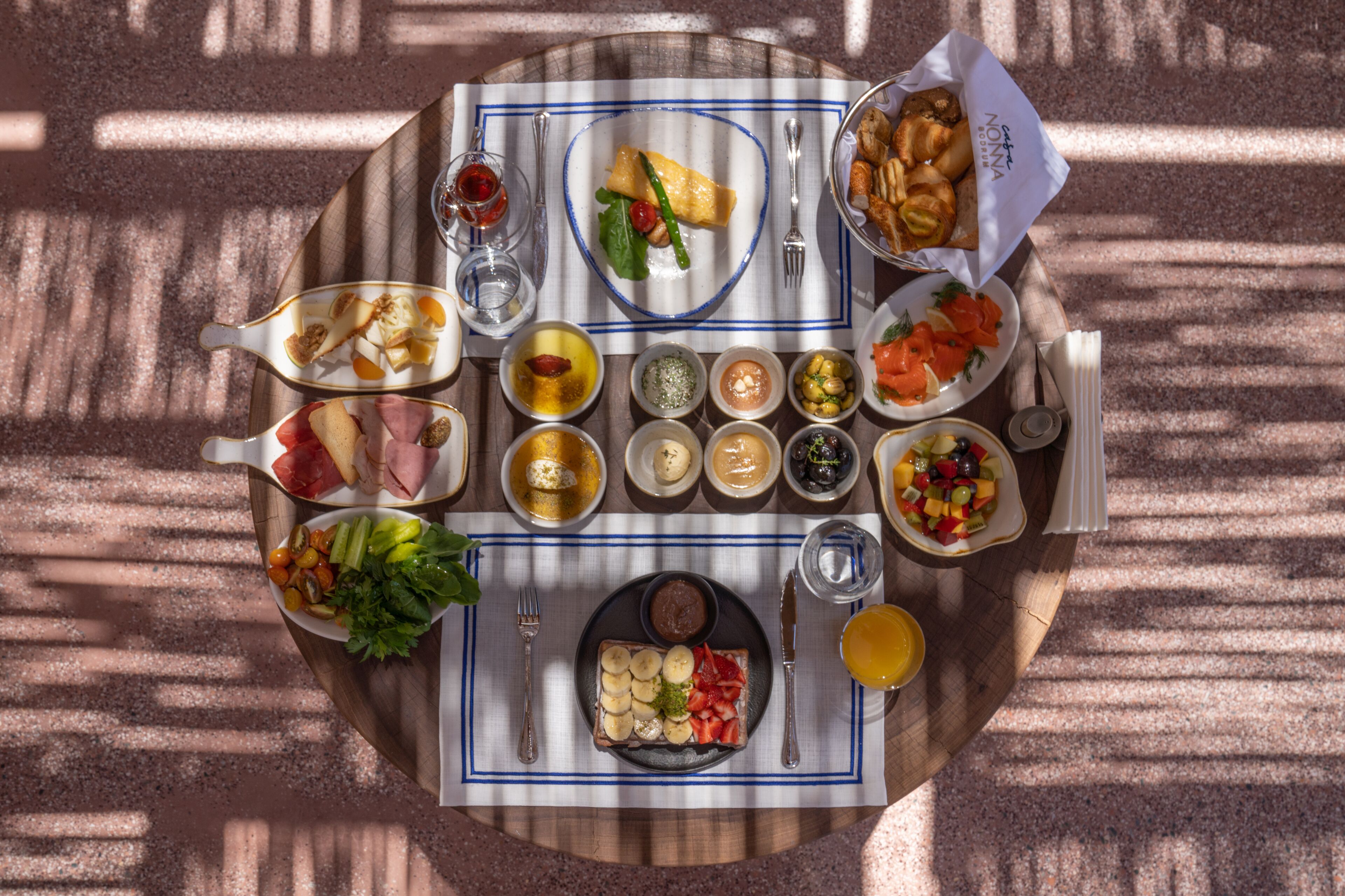 A table set with various dishes, including a plate with sliced bananas and strawberries, a bowl of salad, and a plate of smoked salmon.