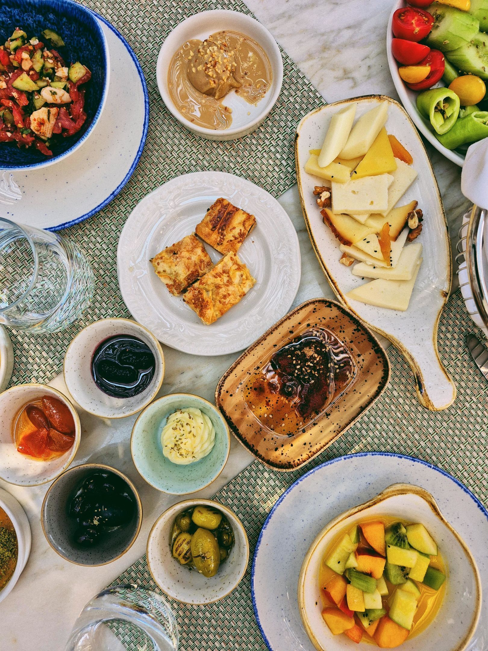 A table set with various dishes, including a bowl of salad, cheese, and fruit.