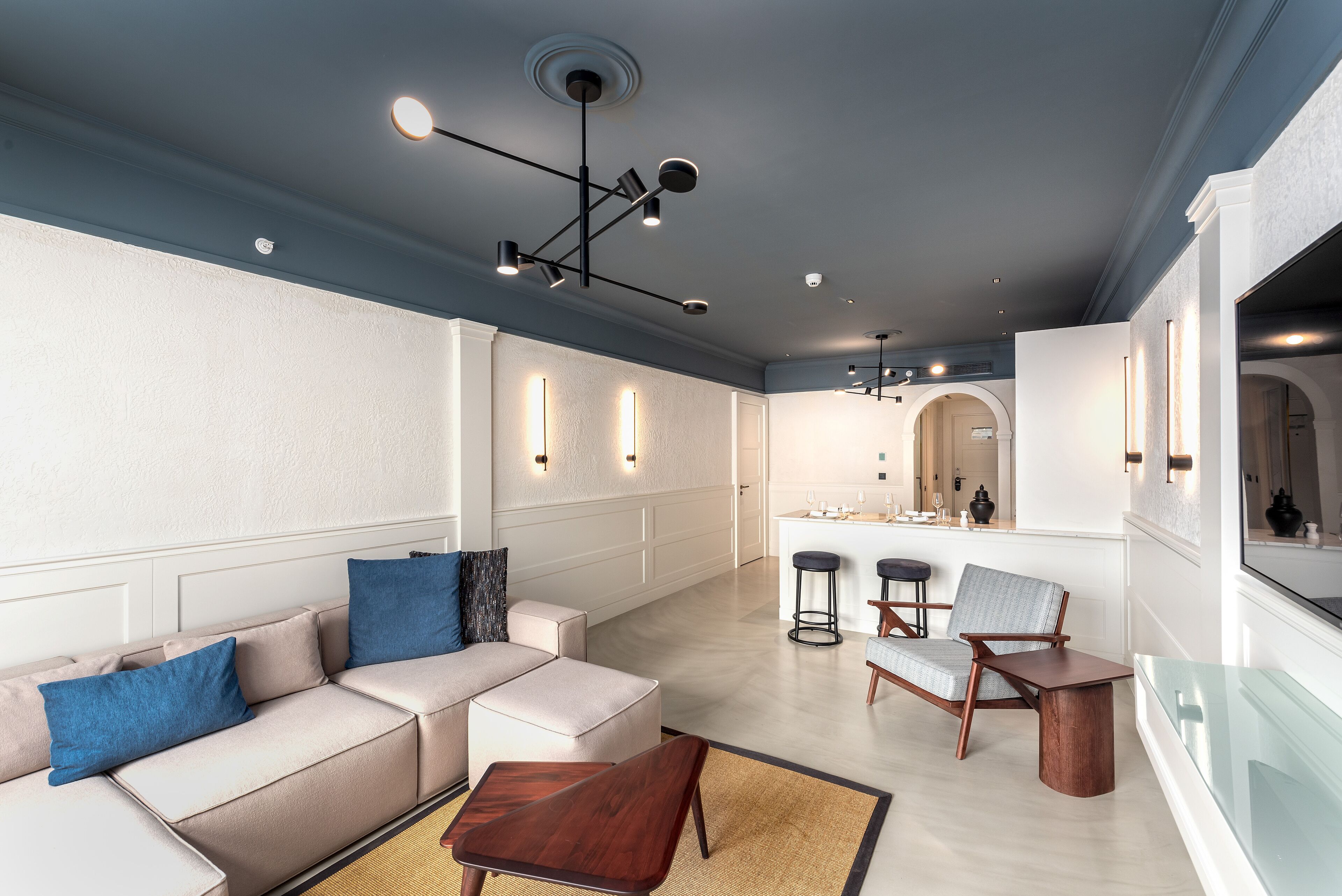 A modern living room with a sofa, chairs, and a coffee table. There is a kitchen area in the background with bar stools and a countertop.