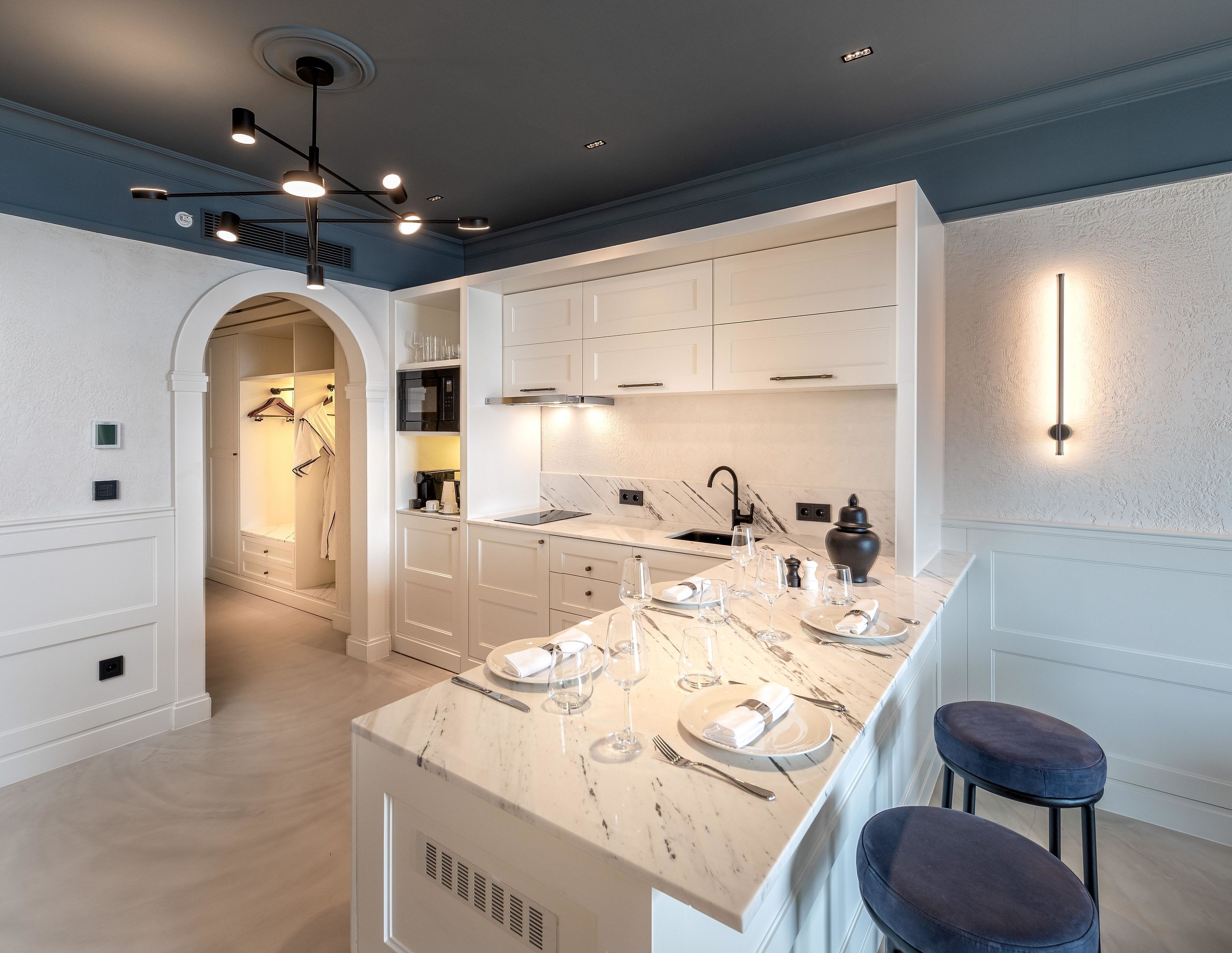 A modern kitchen with white cabinetry, a marble countertop, and a bar area with stools.