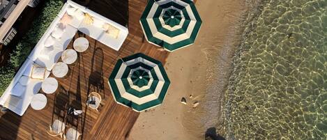 An aerial view of a beachside patio with wooden flooring, white round tables, and green umbrellas.