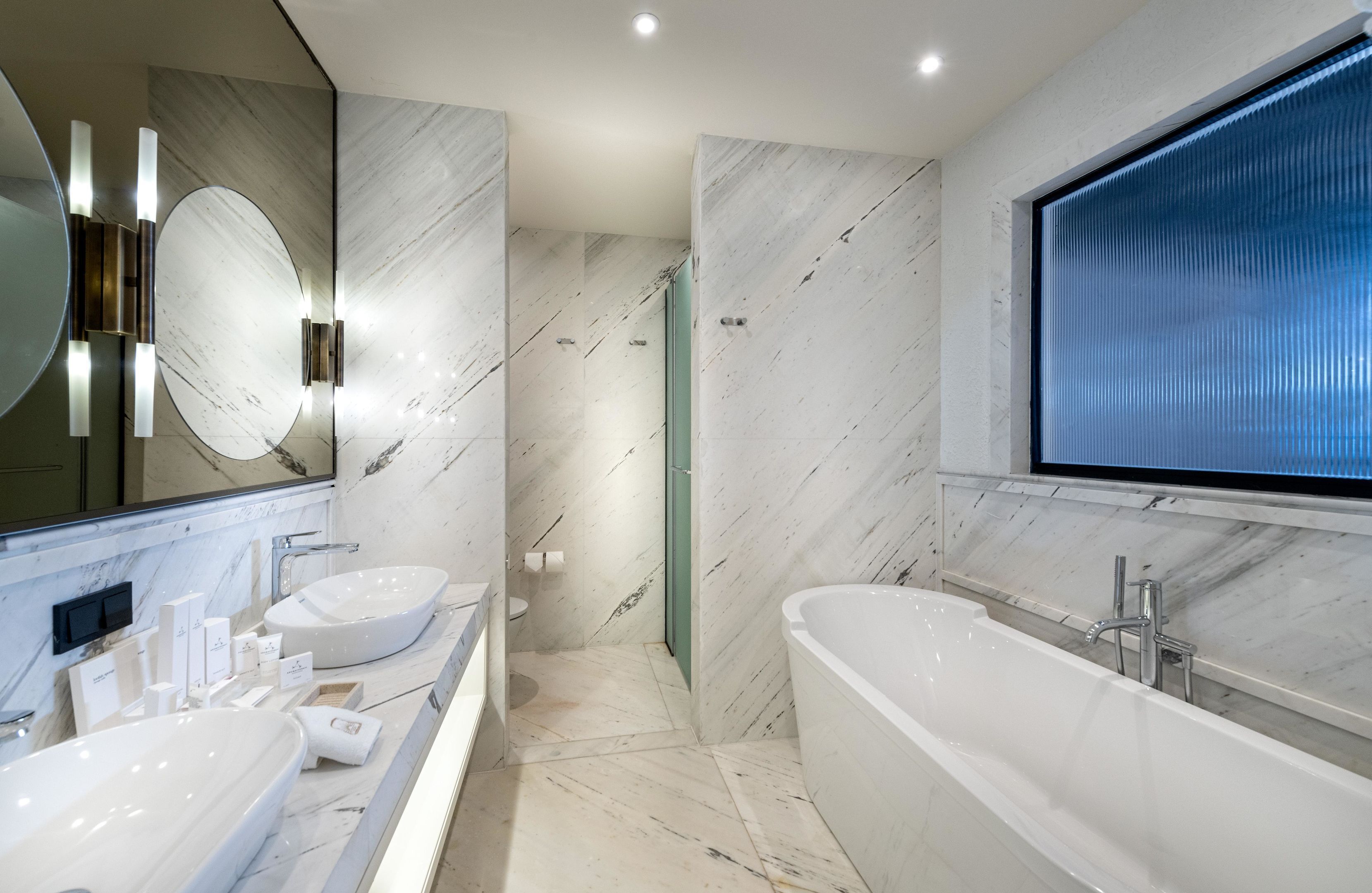 A modern bathroom with a large mirror, two sinks, a bathtub, and a shower.