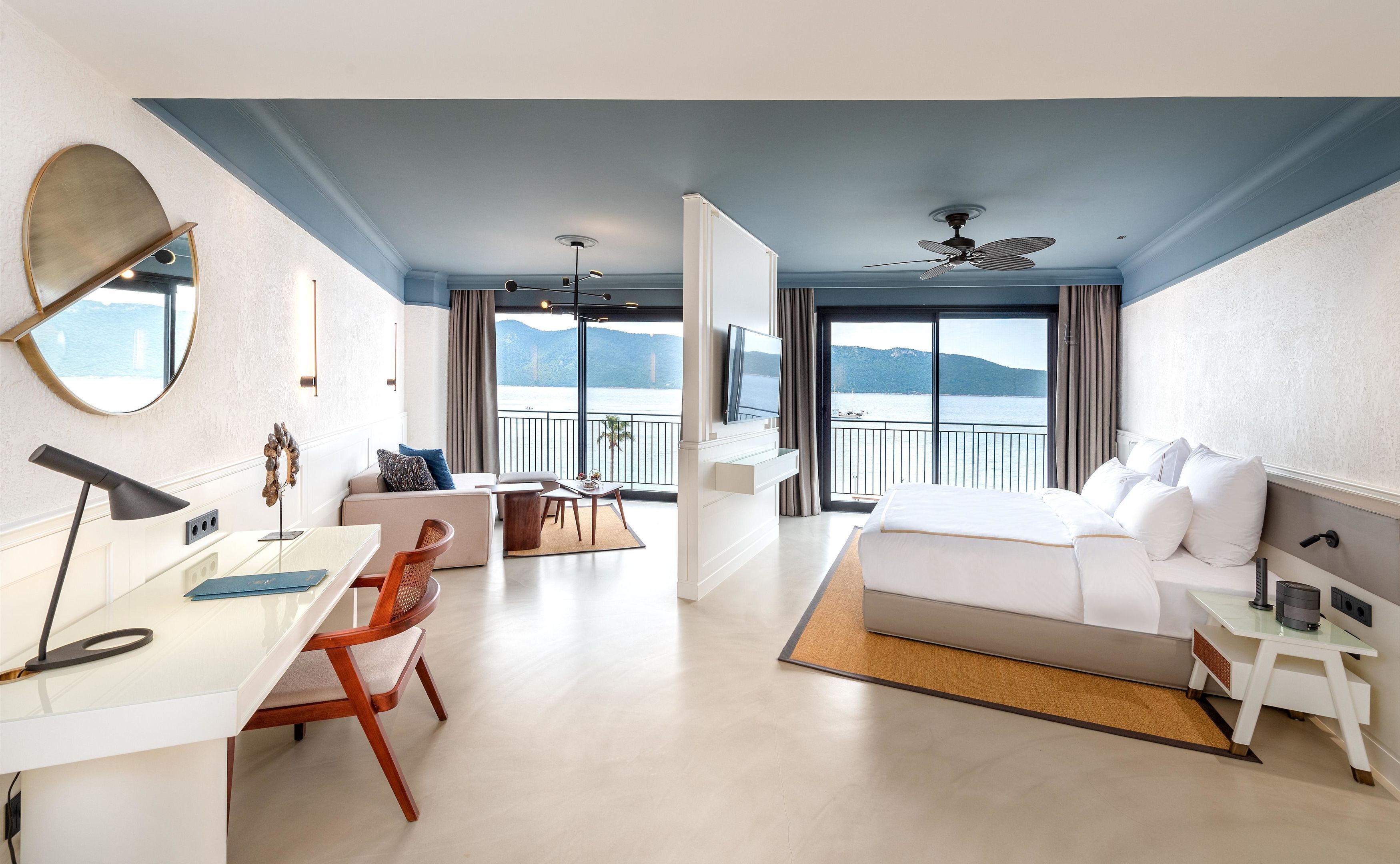 A modern hotel room with a balcony, a bed, a desk, and a chair.