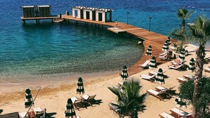 A beach with a wooden pier extending into the sea, lounge chairs, and umbrellas. - Casa Nonna Bodrum - Adult Only (Bodrum)