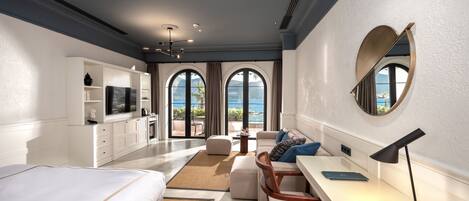 A modern bedroom with a large bed, a desk, and a view of the ocean.